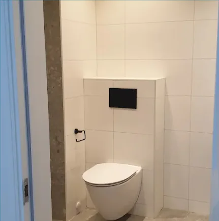 Färdig WC-del med vägghängd toalett och stora ljusa kakelplattor