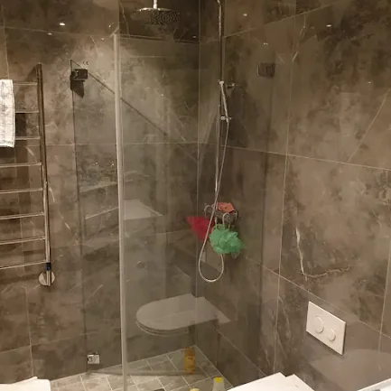 Grå duschzon med glasvägg, takdusch och stora stenplattor