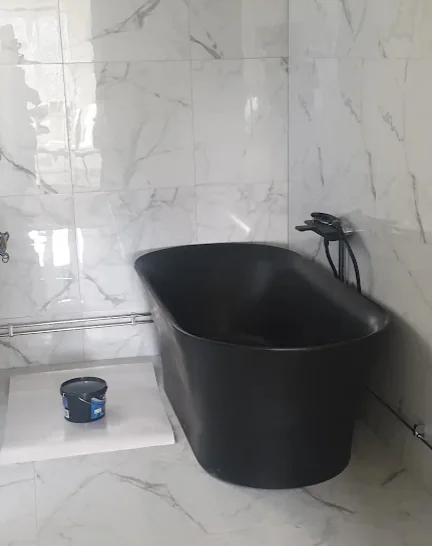 Färdigt ljust badrum med svart fristående badkar och marmorliknande plattor