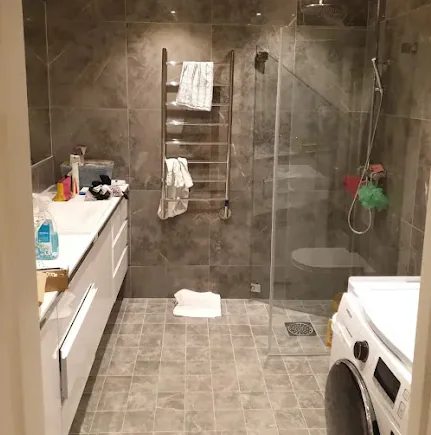 Färdigt grått badrum med duschglas, tvättmaskin och kommod
